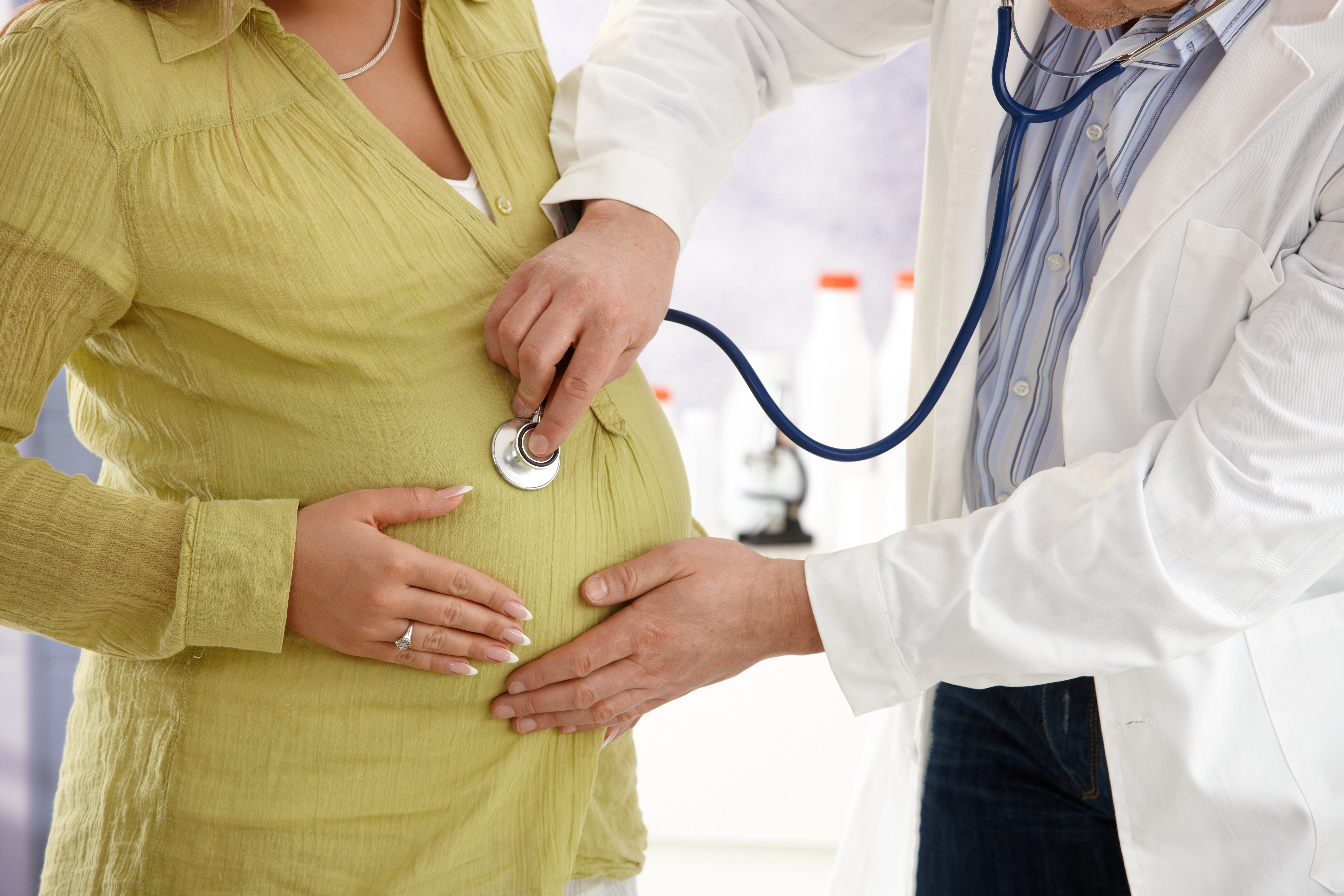 Healthcare provider checking pregnant woman's stomach with stethoscope