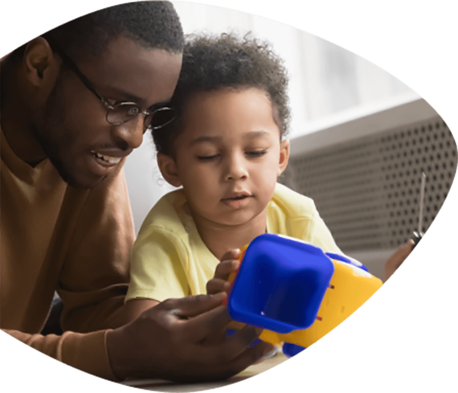 Smiling African American father holding a toy in front of his young son who is looking intently while touching the toy