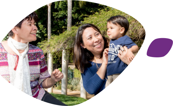 A smiling Asian mother holds her toddler facing his smiling grandmother