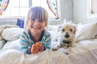little girl sitting with dog on bed